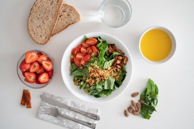 Top view of a healthy salad and fresh ingredients with bread and juice on a white surface.